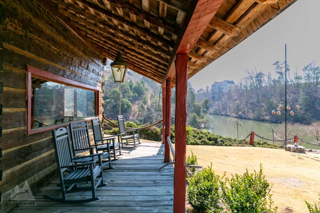 Relaxation awaits on the wooden porch of the Captain's Club's rustic cabin lined with four rocking chairs facing Lake Tuscaloosa, with a hint of spring greenery emerging around the tranquil lake. 